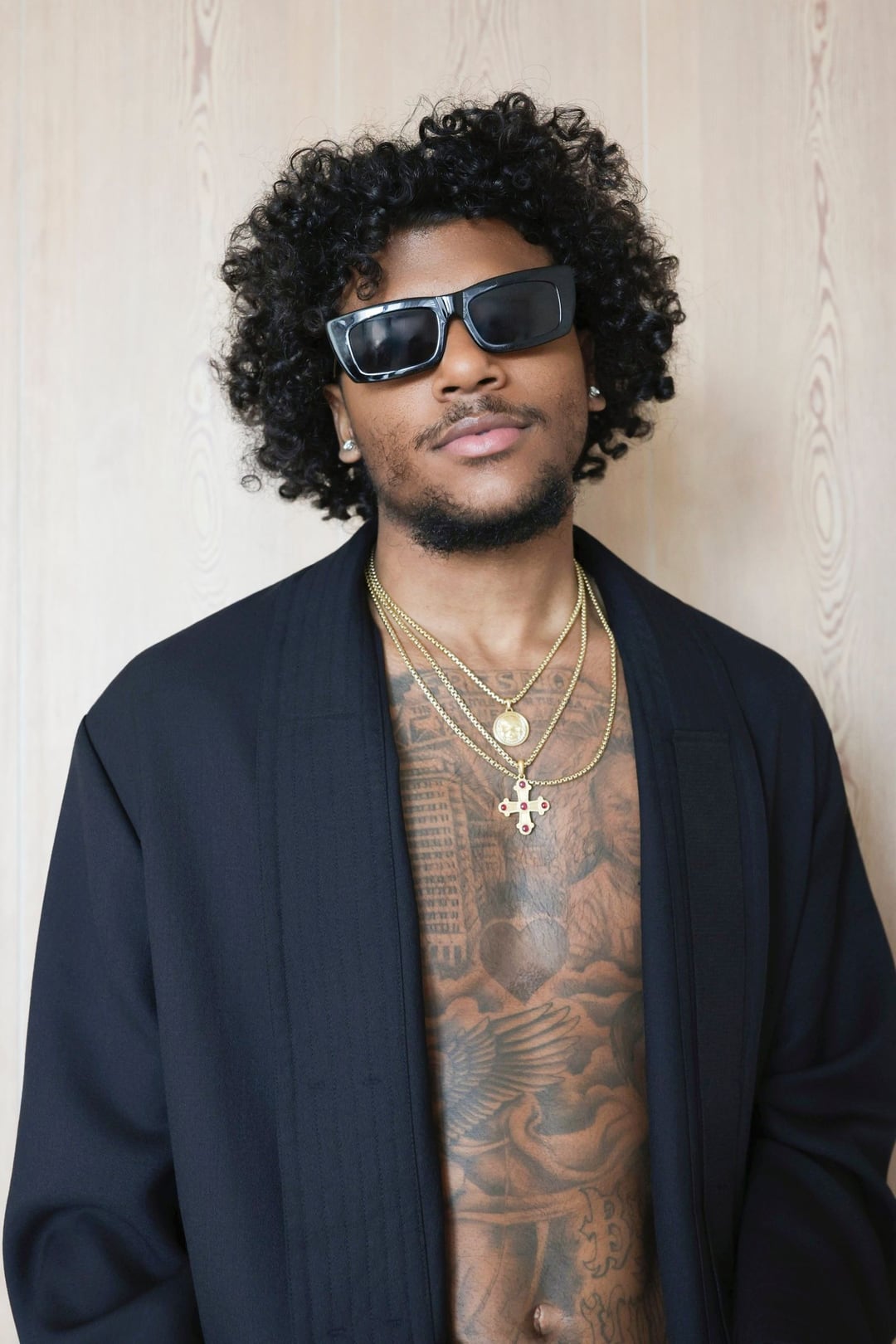 Jalen Green in black sunglasses and an open black jacket over layered gold chains, against pale wood.