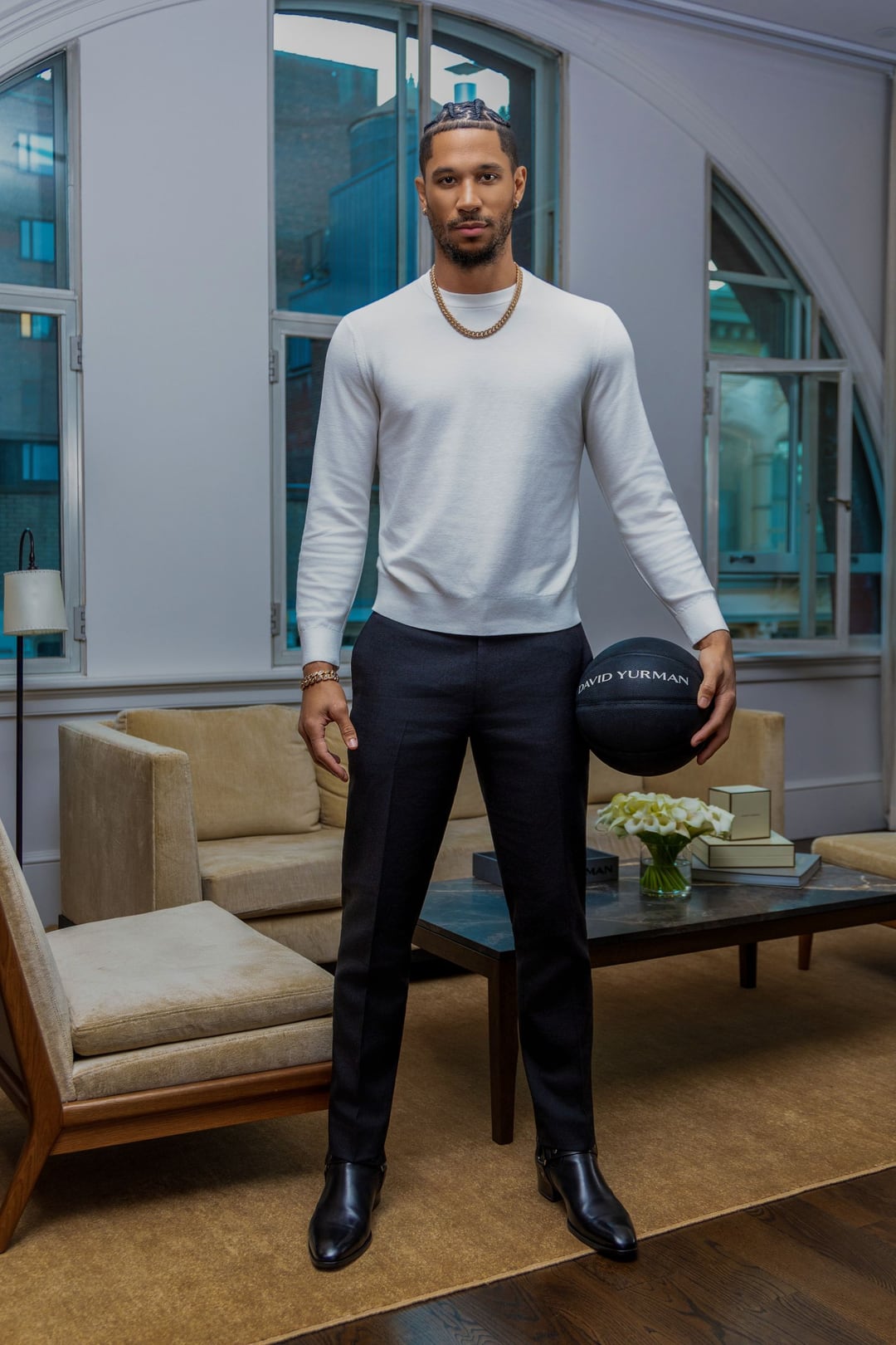 Josh Hart full-length in a hotel suite holding a black basketball, white sweater and black trousers.