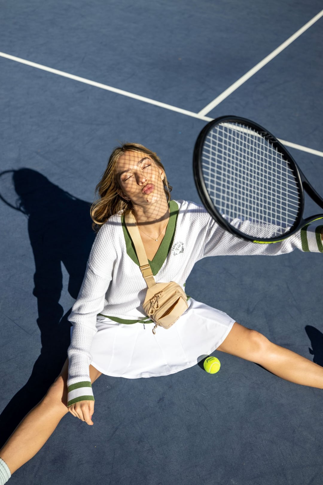 Overhead: a model sprawled on a blue tennis court in whites and a tennis-ball veil, racket beside her.