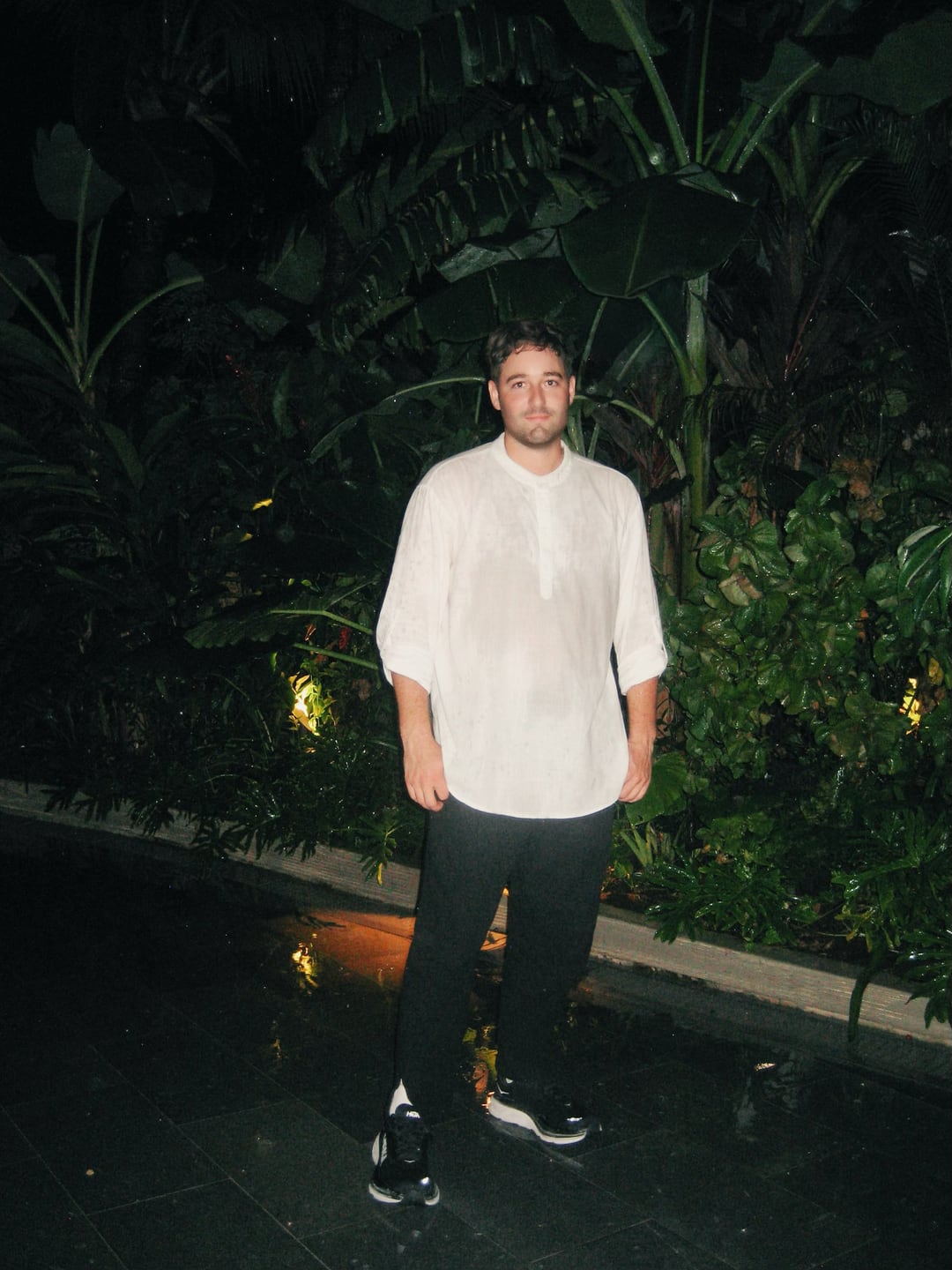 Ryan Houchin at night in Costa Rica, in a white shirt against wet tropical leaves, lit by flash.
